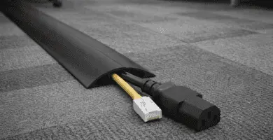 Pasacables de piso de perfil bajo protegiendo cable de alimentación y Ethernet sobre alfombra de oficina.